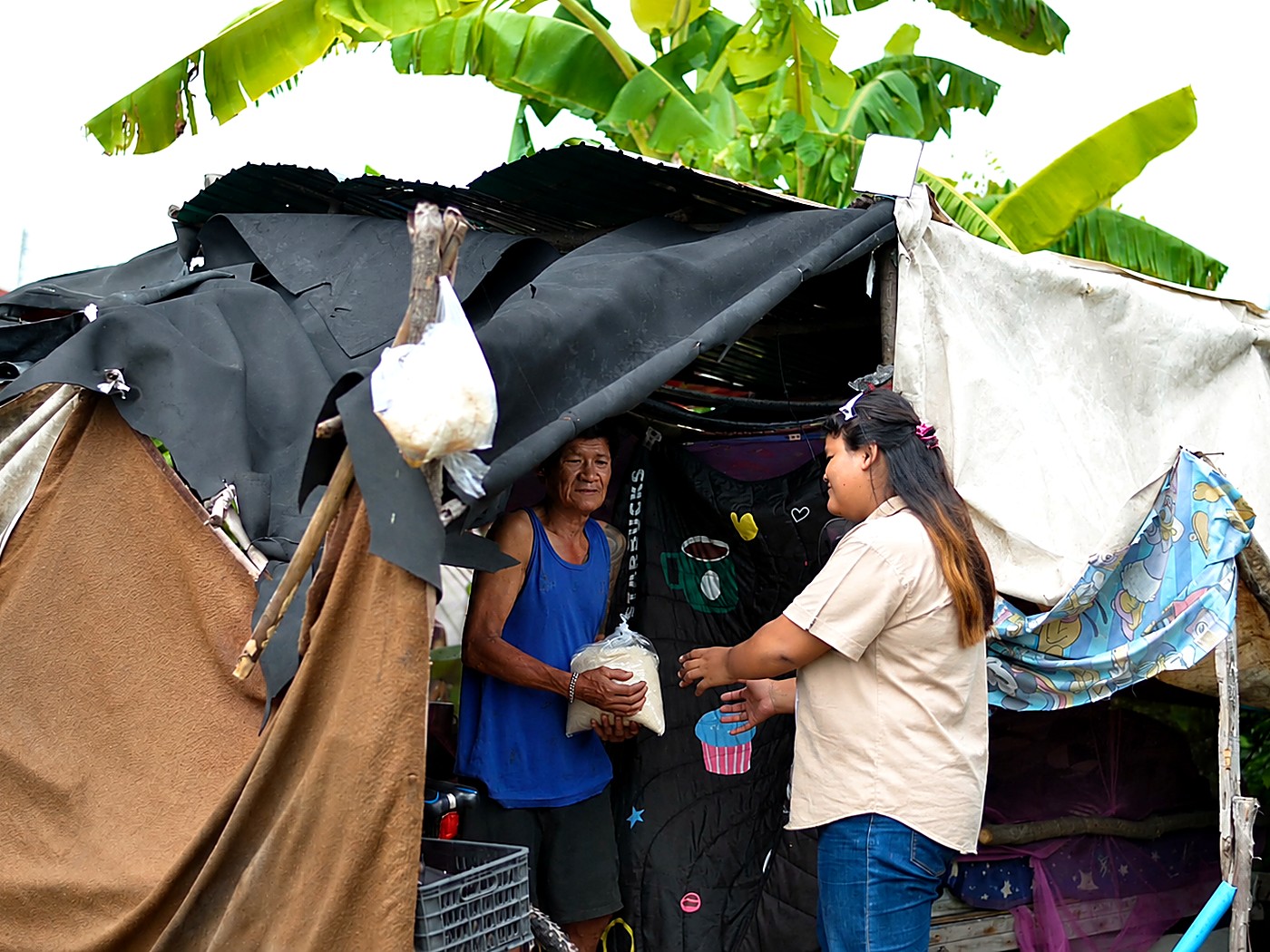 A Hand to Hand volunteer delivering a bag of rice to a man at his home during a family welfare visit