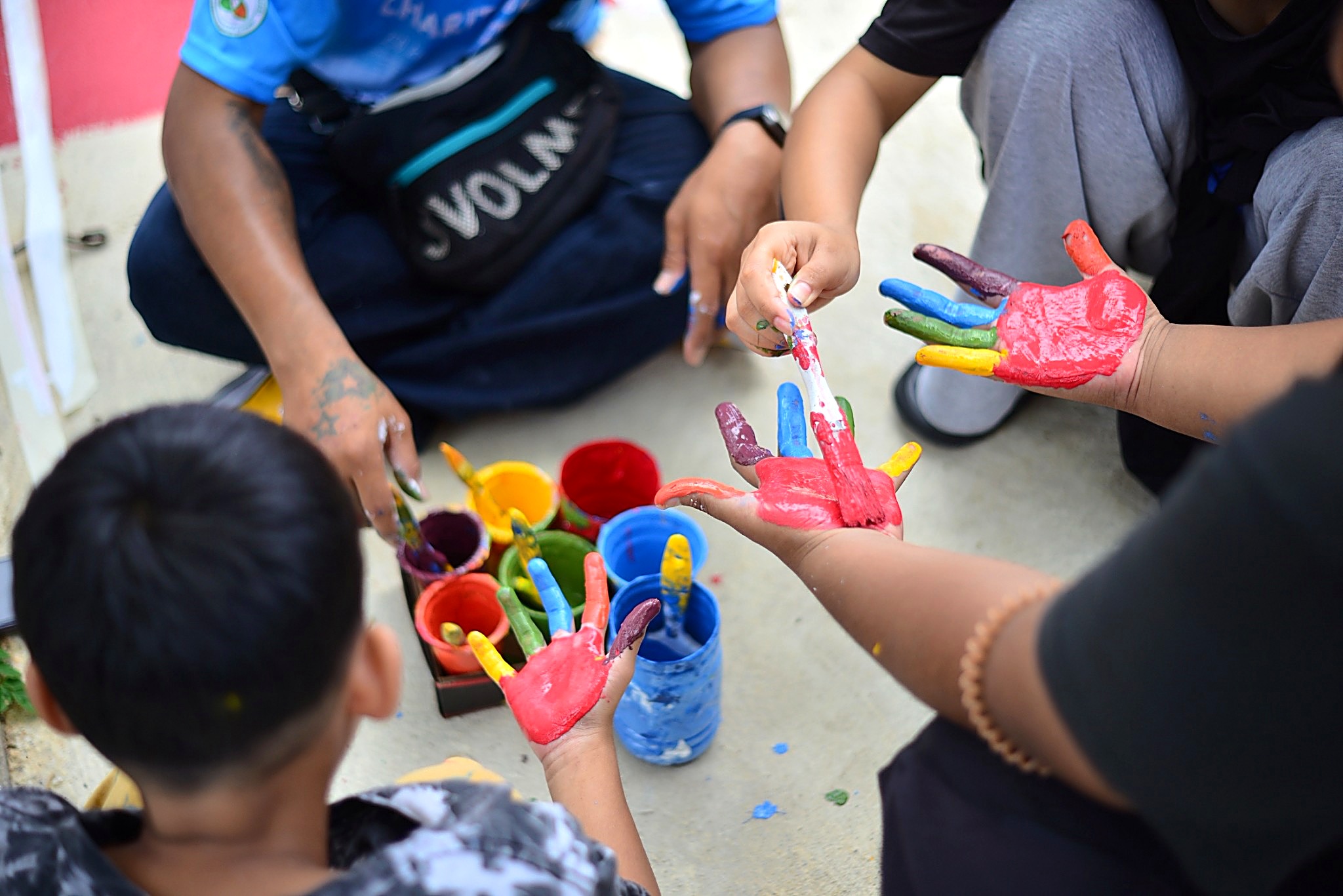 Children and volunteers sharing paint and painting their hands together at a Hand to Hand event