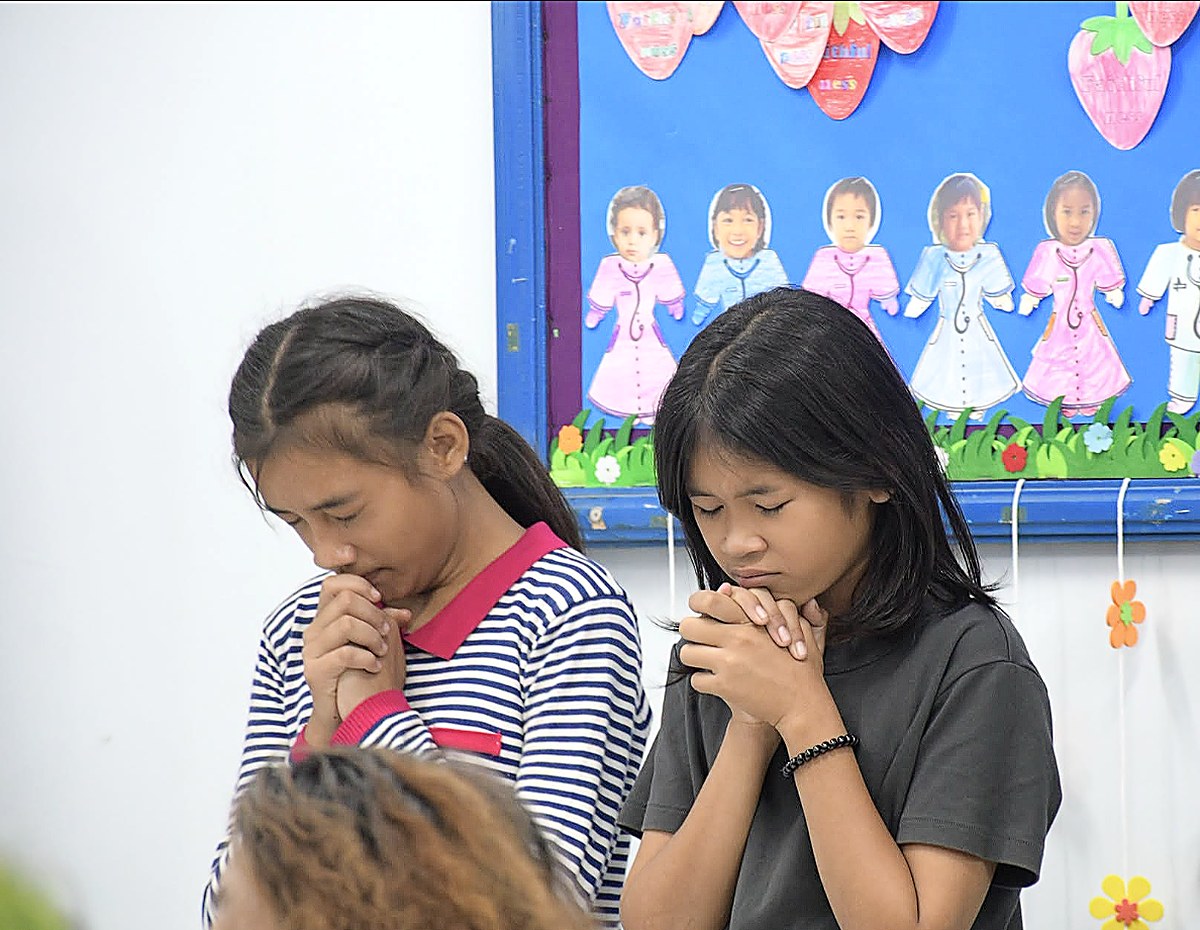 Two girls praying together with hands clasped at a Hand to Hand program