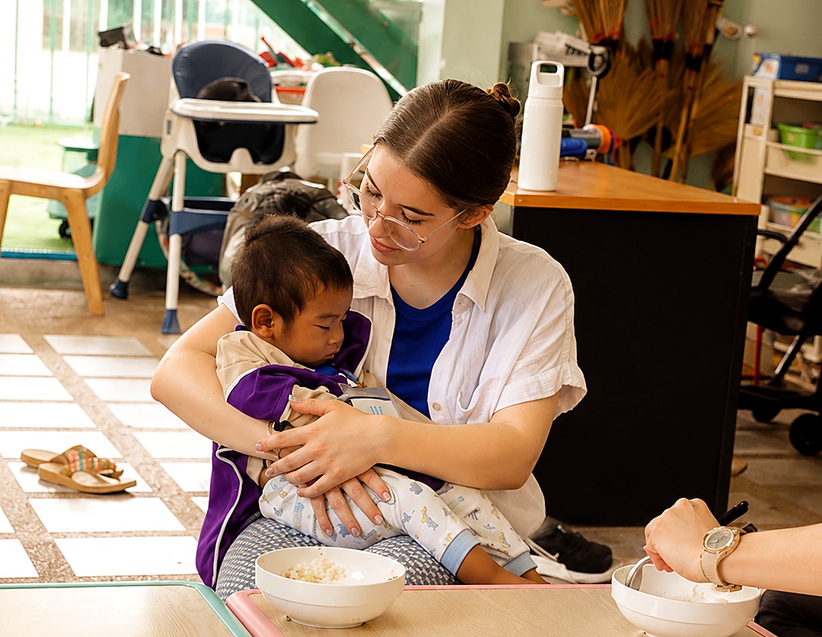 A Hand to Hand volunteer holding and comforting a young child at mealtime